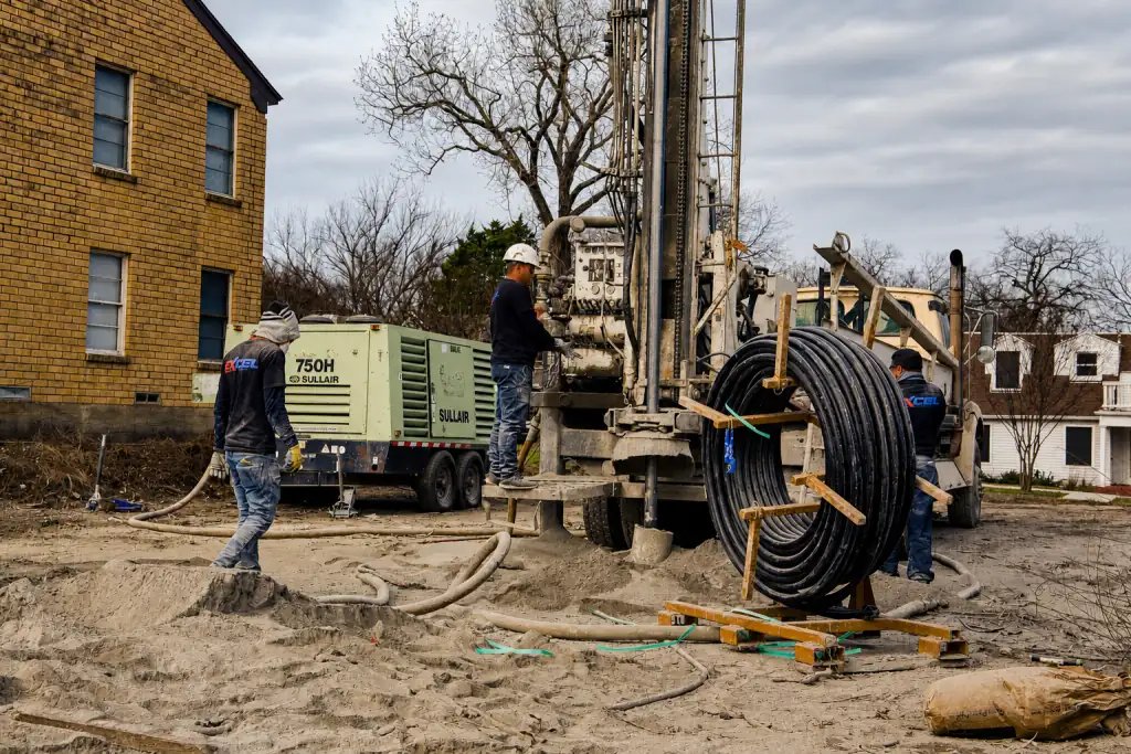 Excel crew drilling a vertical well on a North Texas lot with a reel of loop pipe staged beside the rig