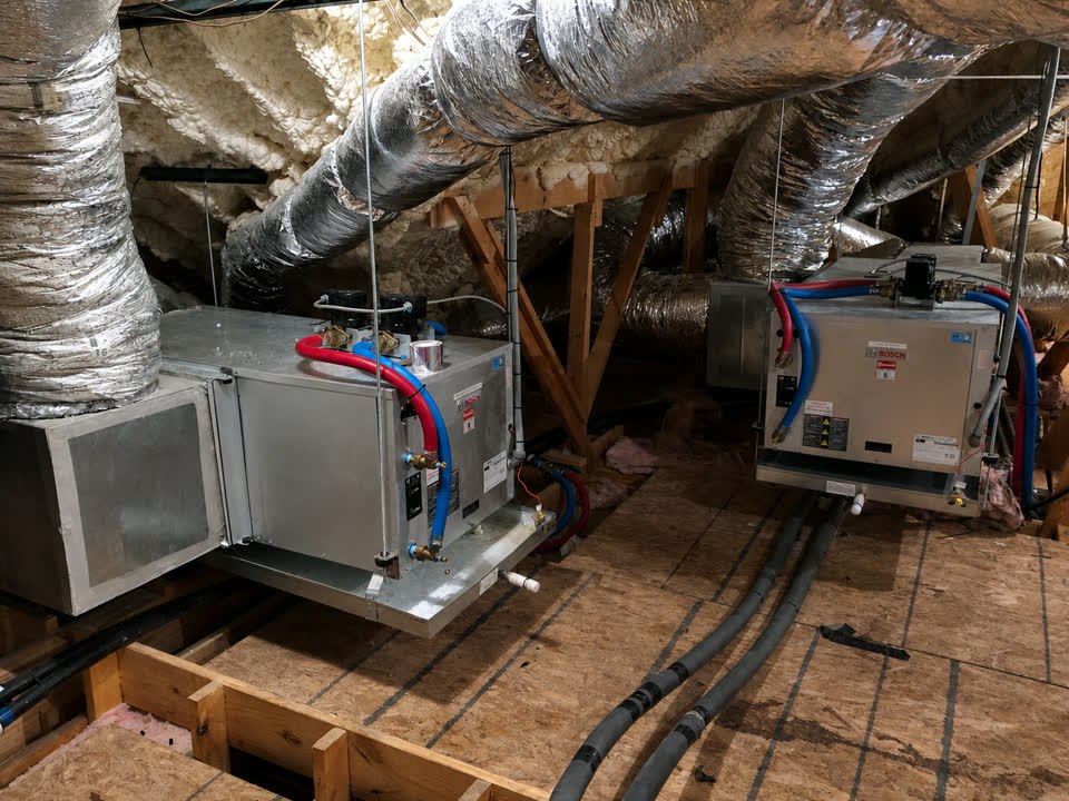 Two Bosch geothermal units suspended in the attic of a McKinney two-story home with insulated ductwork overhead